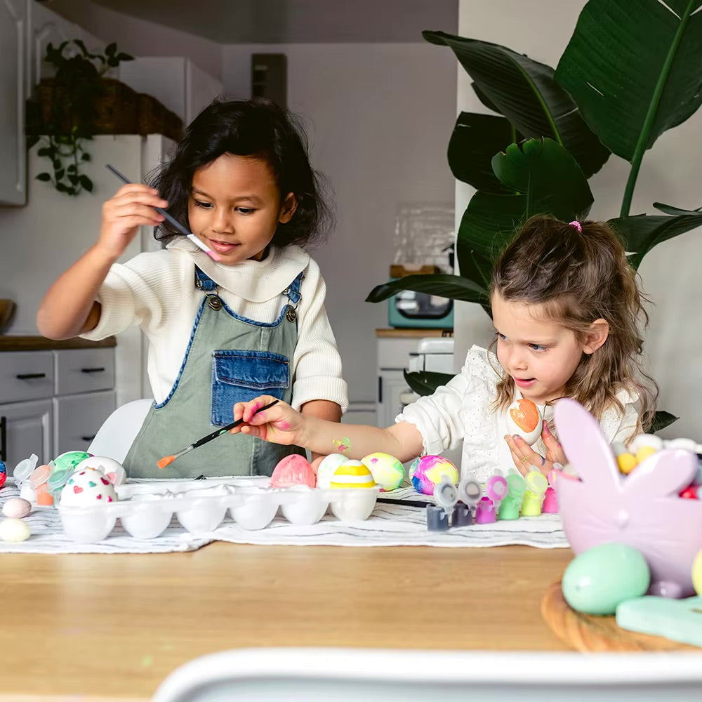 Two kids painting unpainted wooden Easter eggs during a fun DIY craft activity for Easter.