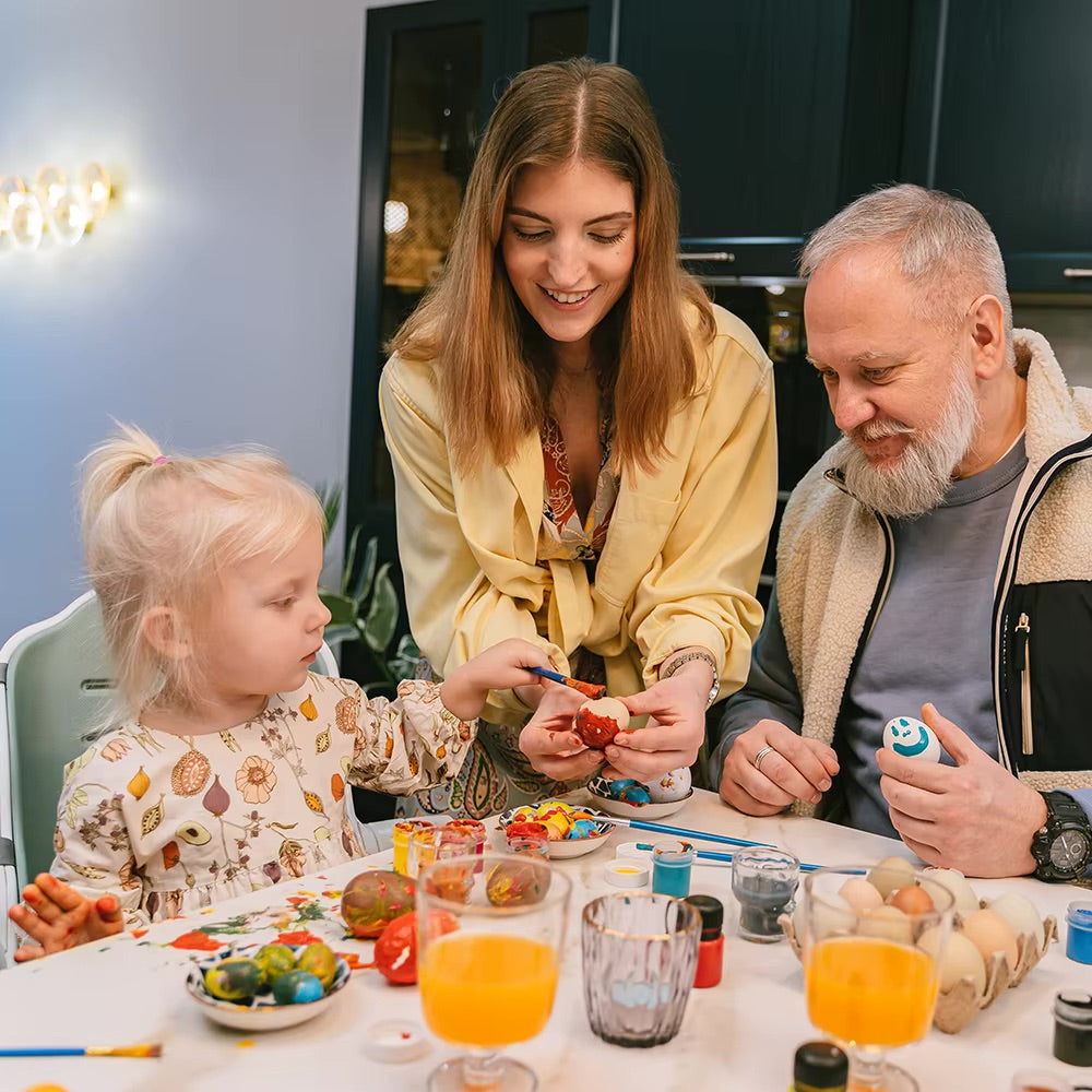 Family enjoying DIY Easter crafts with unpainted wooden eggs and colorful paints at a table.